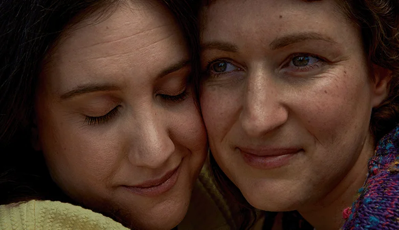 Due donne sorridenti che si abbracciano, mostrando un momento di affetto e intimità.