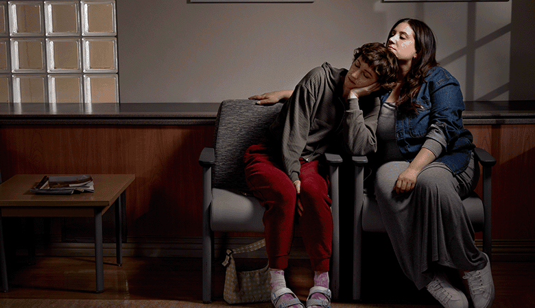 Due persone sedute in una sala d'attesa, una appoggiata all'altra in un gesto di conforto.