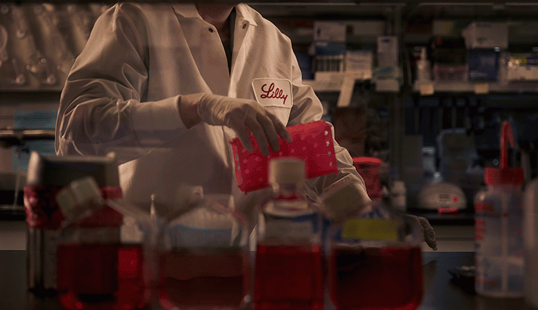 Ricercatore in laboratorio che lavora con campioni in contenitori rossi, indossando un camice bianco.